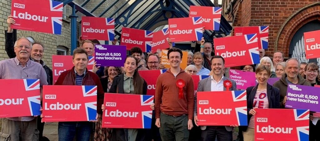 Lets prove there are ‘NO no-go zones for Labour’ says Luke Viner Labour candidate Luke Viner aims to win in South Cambridgeshire and to “build on the string of Labour victories in blue-wall seats, we can prove there are NO no-go zones for Labour”. Luke, chair of South Cambridgeshire Labour and a Fulbourn parish councillor, is hoping voters will back someone who has “lived and breathed this constituency my entire professional life”. On Bank Holiday Monday Luke drew a sizeable crowd to a packed event at Sawston Free Church. He was supported by Labour fellow parliamentary candidates Elizabeth McWilliams (Ely & East Cambridgeshire), Alex Bulat (Huntingdon) and Kevin Bonovia (Stevenage), and Labour’s Combined Authority Mayor Dr Nik Johnson. Luke explained what the Labour Party means to him and why he is standing to be elected as an MP. “I was born under the last Labour government, and received my early education under it,” he said. “It gave me a great start, a passion for learning, including my love of music. Things worked then. You could see a doctor within 48 hours. Class sizes were under 30 and teachers were well respected. The economy had a long period of strong growth. “However, since the Tories were elected, enabled for the first five years by the Lib Dems, things have gone downhill. “Austerity brought terrible hardship and long-lasting damage to our services including the NHS, education, and local council services. “Nowhere near enough houses have been built, particularly truly affordable including social housing. Our economy has been wrecked by Tory incompetence. We are poorer, more taxed than ever before and what do we have to show for it?” He added: “I want to be elected so that I can represent the people of South Cambridgeshire at the very heart of a Labour government that is once again back in the service of the British people. “A government that would work to return the country to how it should be run, cutting waiting lists, increasing the number of teachers, increasing the numbers of police officers on the beat, building 1.5 million new homes including many truly affordable homes and growing the economy.” Mayor Johnson said: “Luke is very impressive. He is hugely energetic, very smart, and totally committed to do the very best for the community has called home for five years. “He understands the importance of cooperation, community and compassion and he would make a great MP for South Cambridgeshire.” Luke Viner at a Labour rally on Monday supported by Labour fellow parliamentary candidates Elizabeth McWilliams (Ely & East Cambridgeshire), Alex Bulat (Huntingdon) and Kevin Bonovia (Stevenage), and Labour’s Combined Authority Mayor Dr Nik Johnson.